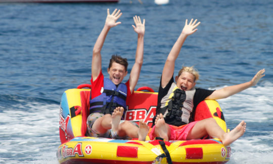 campers seated on a tube being pulled by a boat